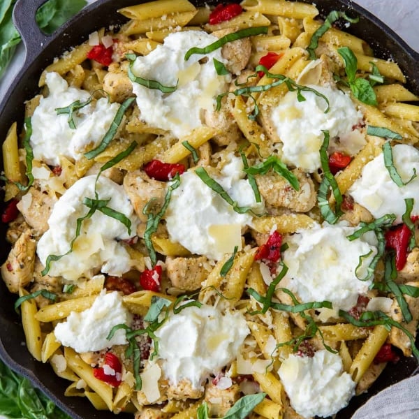 A cast iron skillet filled with pasta topped with scoops of ricotta cheese.