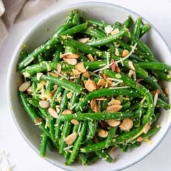 An over the top shot of Pesto Green Beans with almonds next to a grey cloth.