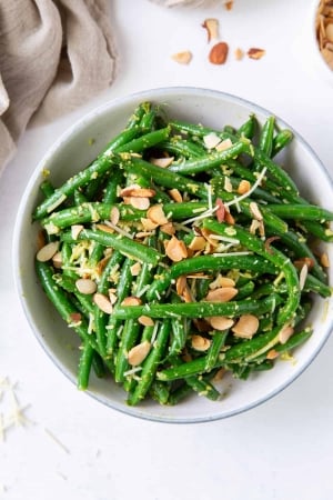 An over the top shot of Pesto Green Beans with almonds next to a grey cloth.