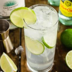 A Ranch Water cocktail in a tall glass with ice and lime slices.