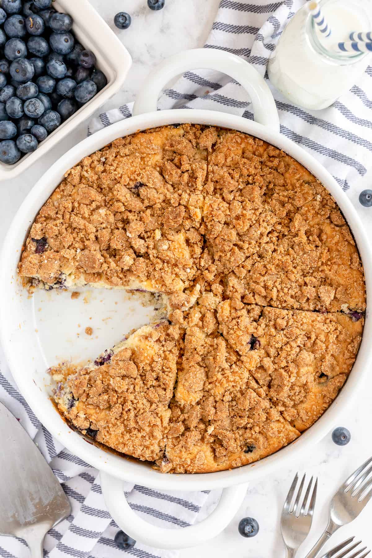 An over the top shot of a crumb cake in a round dish with a piece missing.