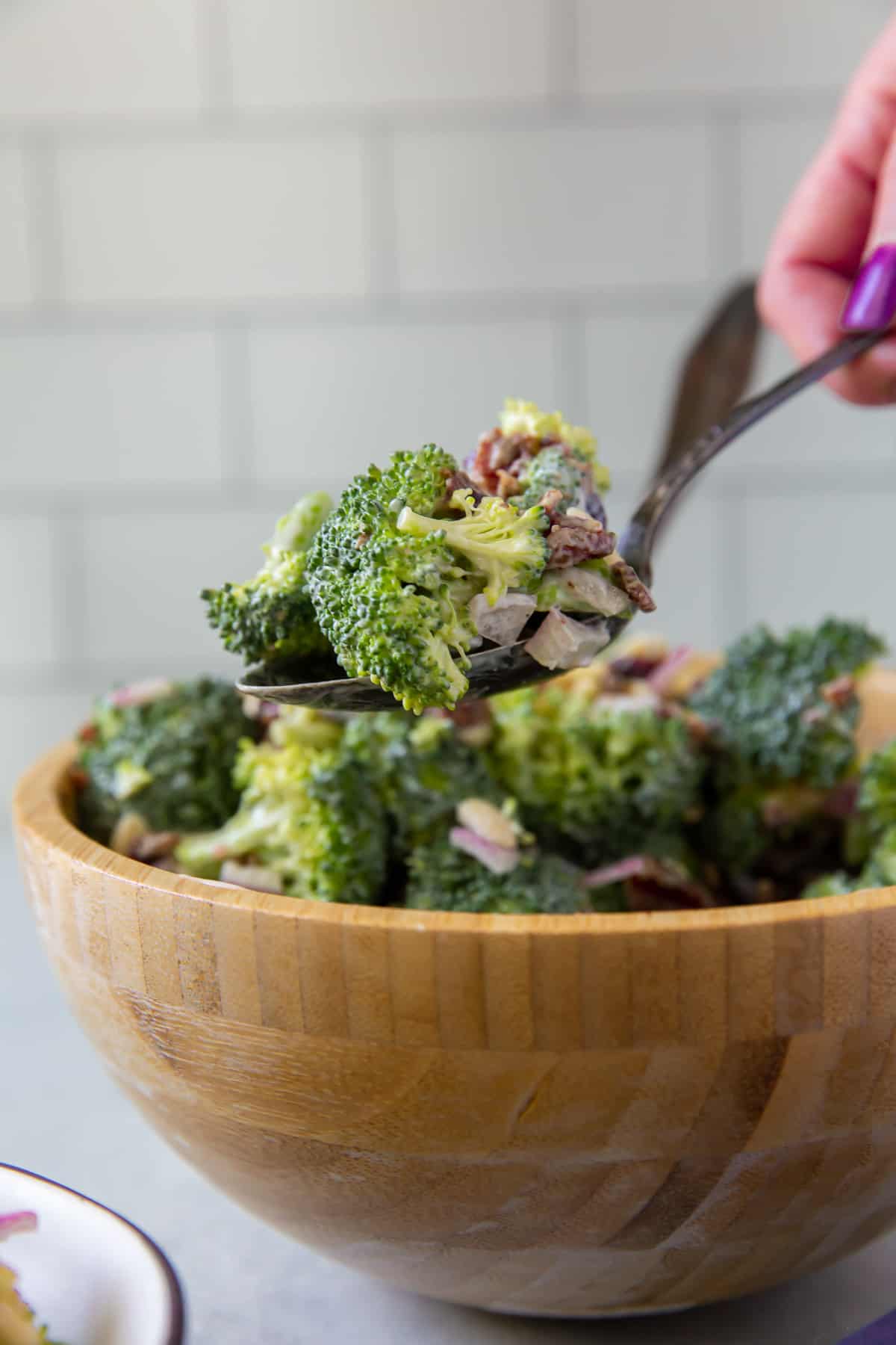 A spoon lifts a scoop of Broccoli Salad from a wooden bowl.