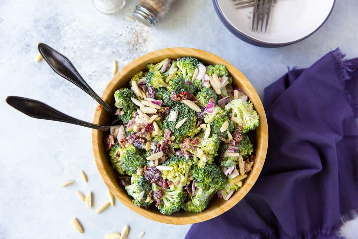 An over the top shot of a bowl of Broccoli Salad next to a purple cloth.