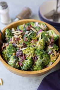 A wooden bowl full of Broccoli Salad with salt and pepper shakers in the background.