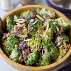 A wooden bowl full of Broccoli Salad with salt and pepper shakers in the background.