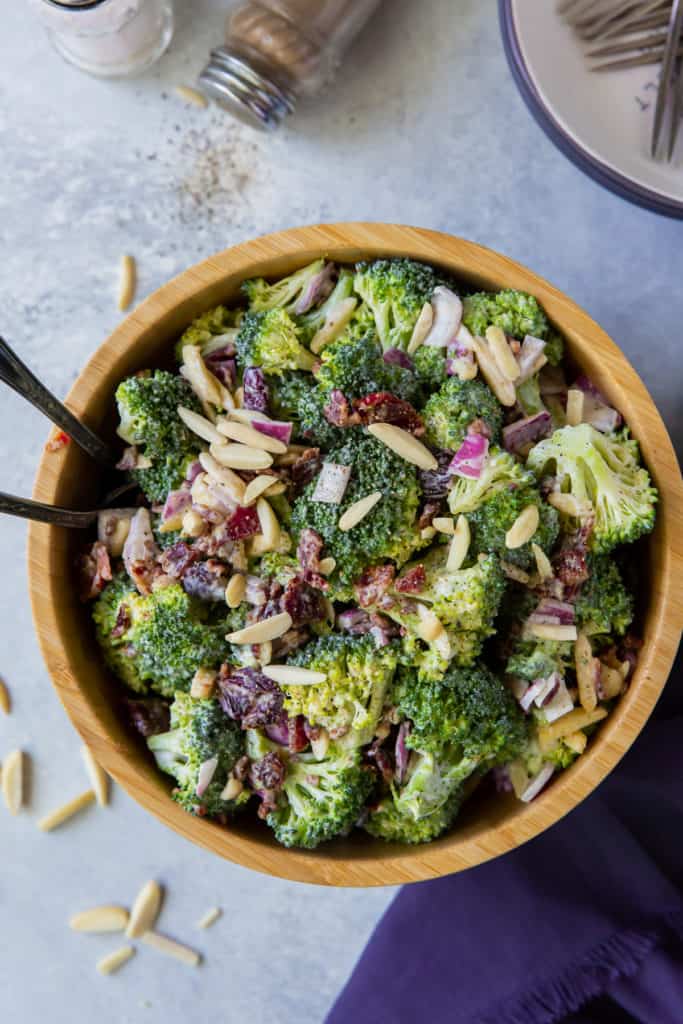 An over the top shot of a bowl of Broccoli Salad next to a purple cloth.