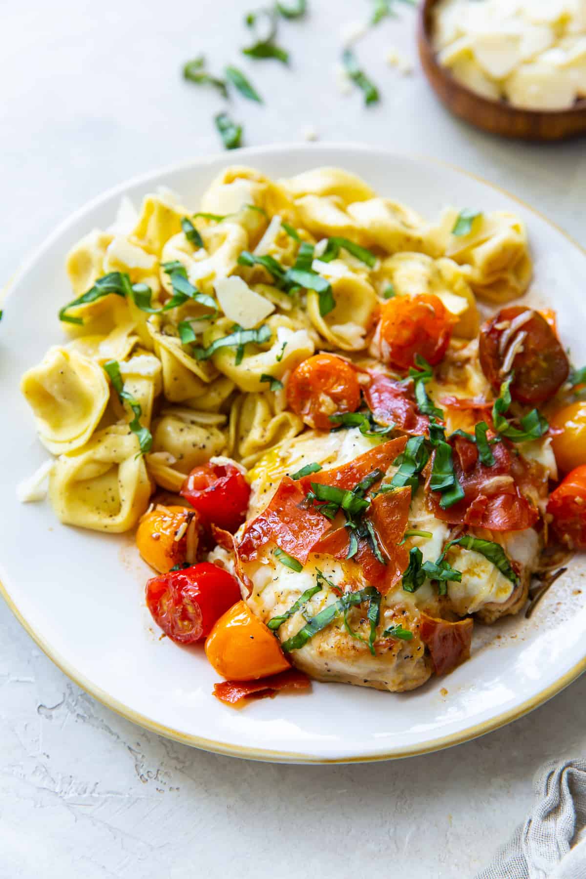 Caprese Chicken on a white dinner plate with tortellini.