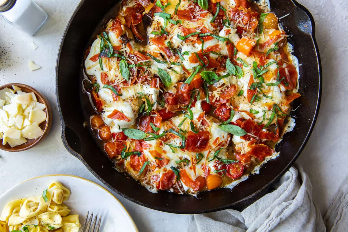 An over the top shot of Caprese Chicken in a cast iron skillet.