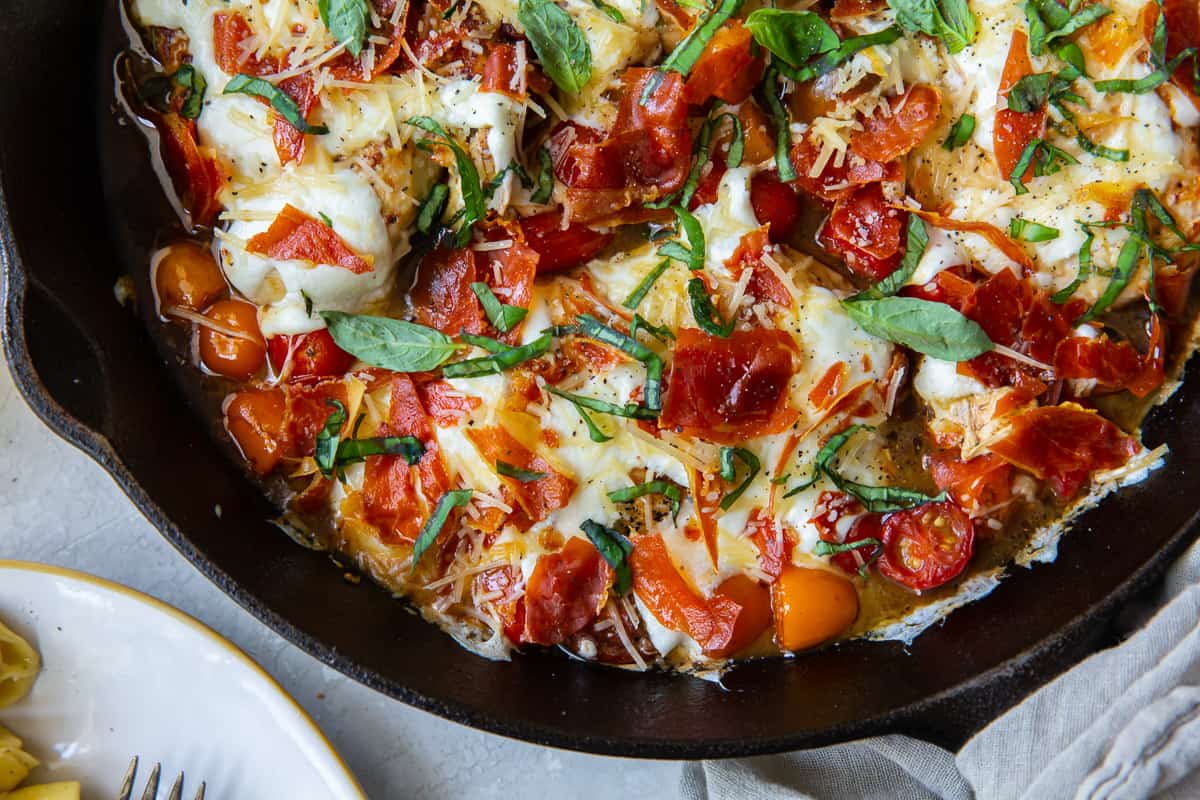 A close up of chicken in a tomato sauce with mozzarella in a skillet.