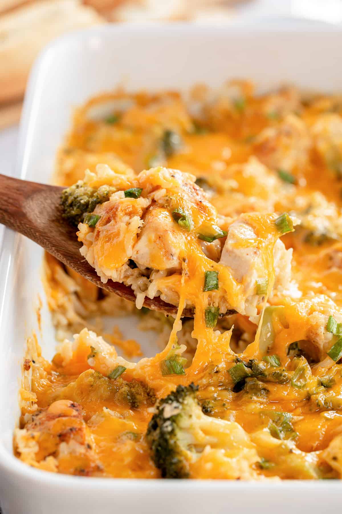 A spoon scoops Chicken Broccoli Rice Casserole from a baking dish.