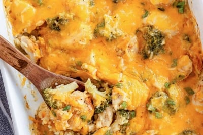 An over the top shot of a spoon resting in a casserole dish full of Chicken Broccoli Rice Casserole.