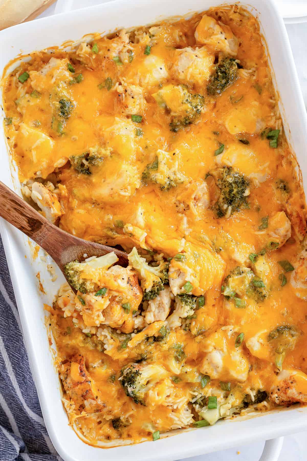 An over the top shot of a spoon resting in a casserole dish full of Chicken Broccoli Rice Casserole.