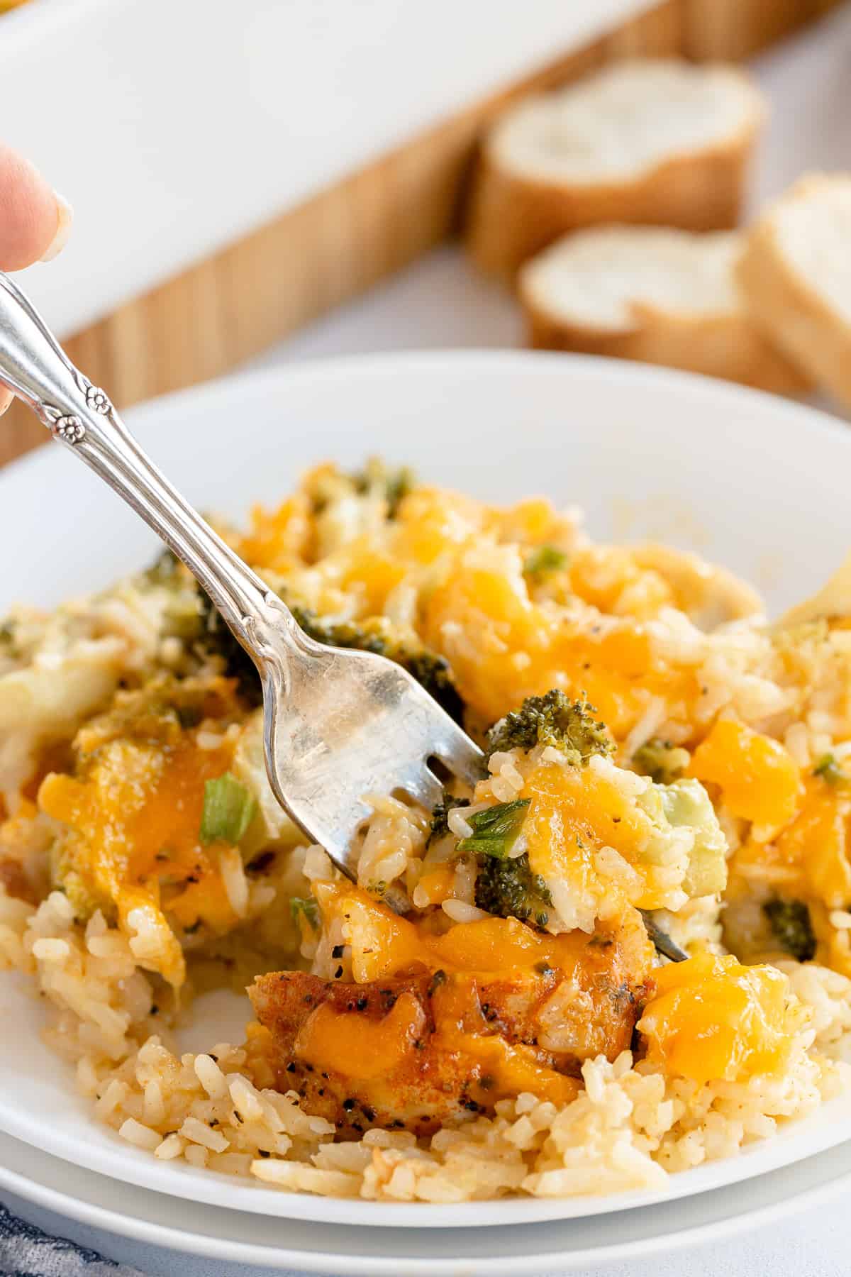 A fork digs into a serving of Chicken Broccoli Rice Casserole on a white dinner plate.