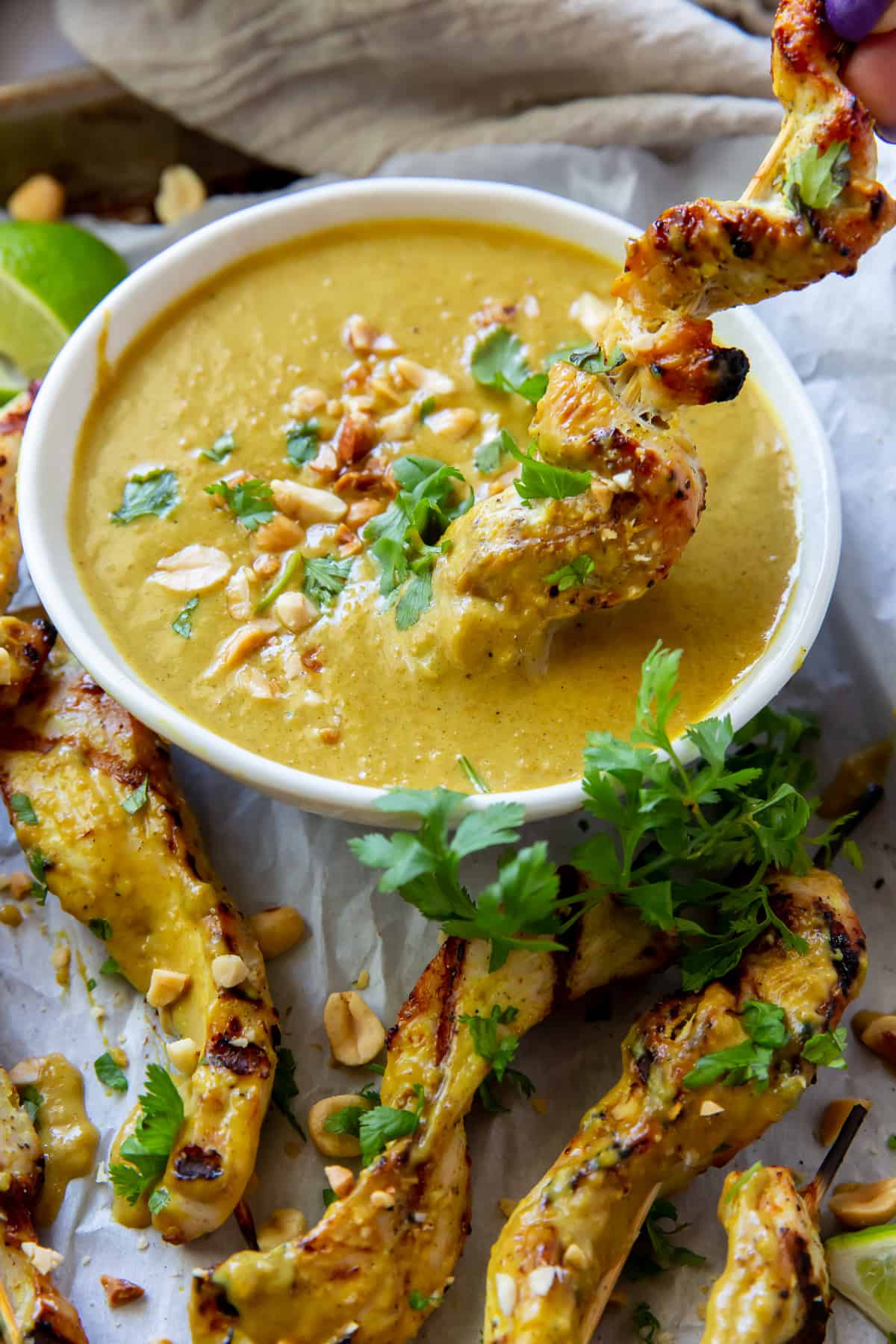 A chicken skewer being dipped into a bowl of peanut sauce.