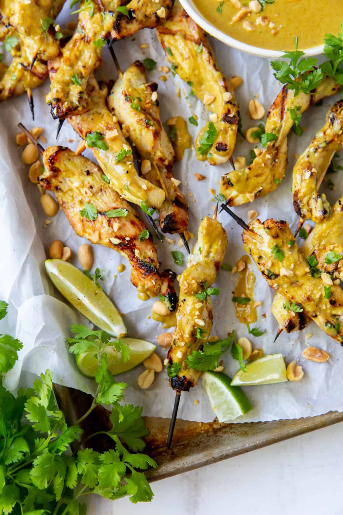 An over the top shot of a baking sheet filled with chicken satay with cilantro and lime.