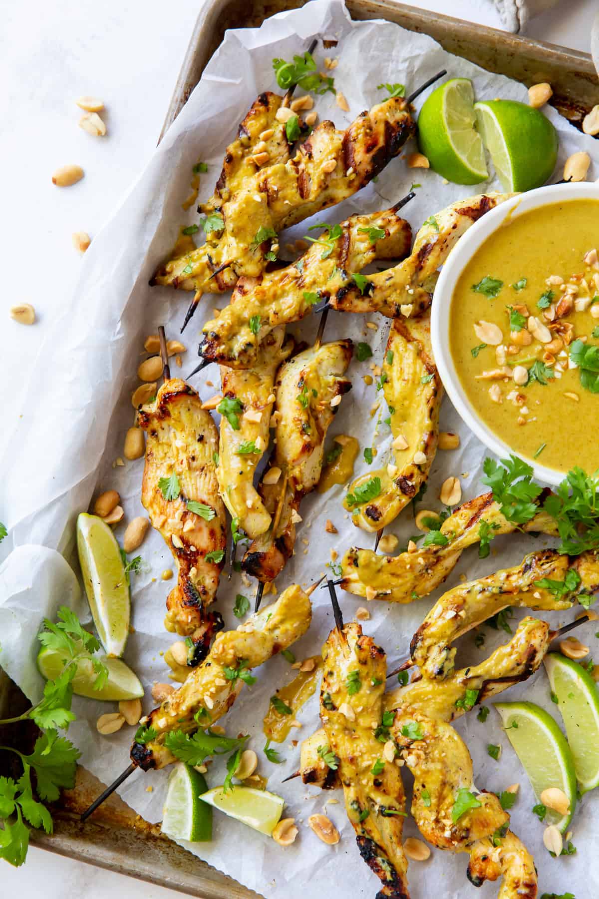 An over the top shot of Grilled Chicken Satay skewers on a baking sheet with cilantro and lime.