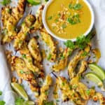 An over the top shot of Chicken Satay on a baking sheet with a bowl of peanut sauce.
