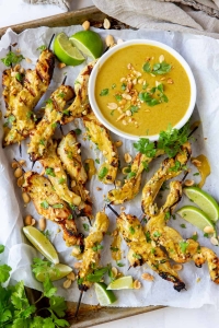 An over the top shot of Chicken Satay on a baking sheet with a bowl of peanut sauce.