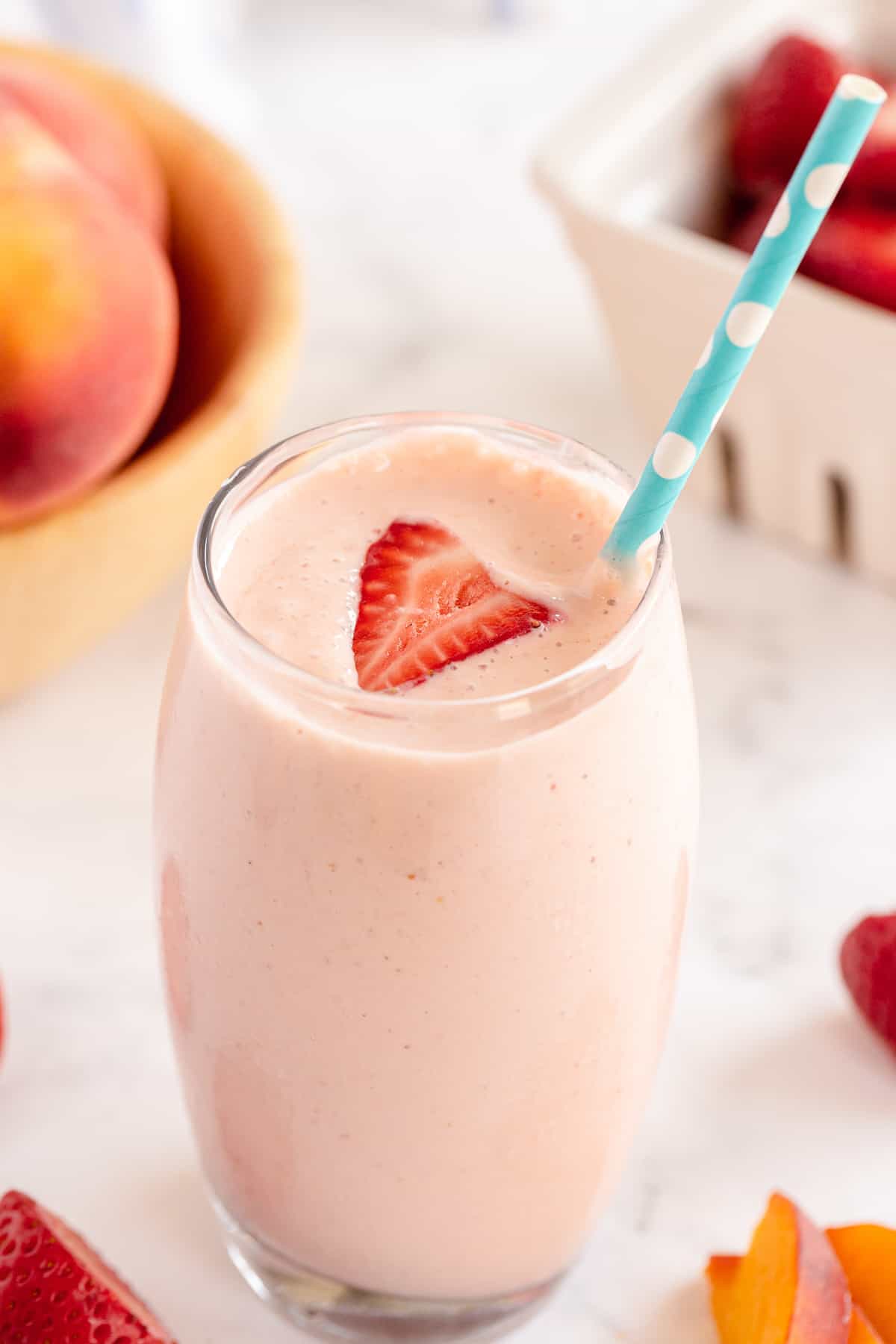 A Strawberry Peach Smoothie topped with a slice of strawberry in a glass with a straw.