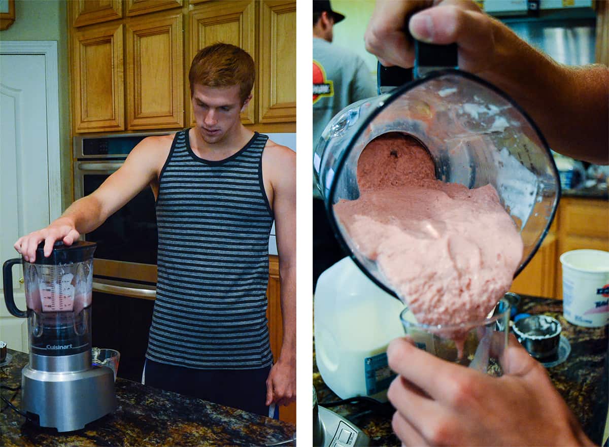 A young man standing at a kitchen counter making a smoothie in a blender.