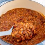 A spoon scoops baked beans from a Dutch oven.