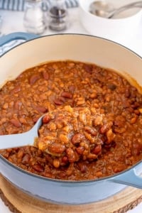 A spoon scoops baked beans from a Dutch oven.