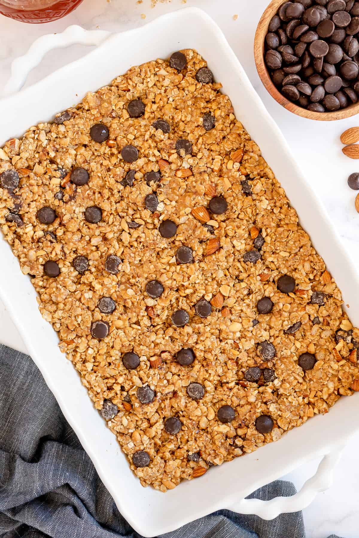 An over the top shot of No Bake Granola Bars in a white dish next to a small bowl of chocolate chips.