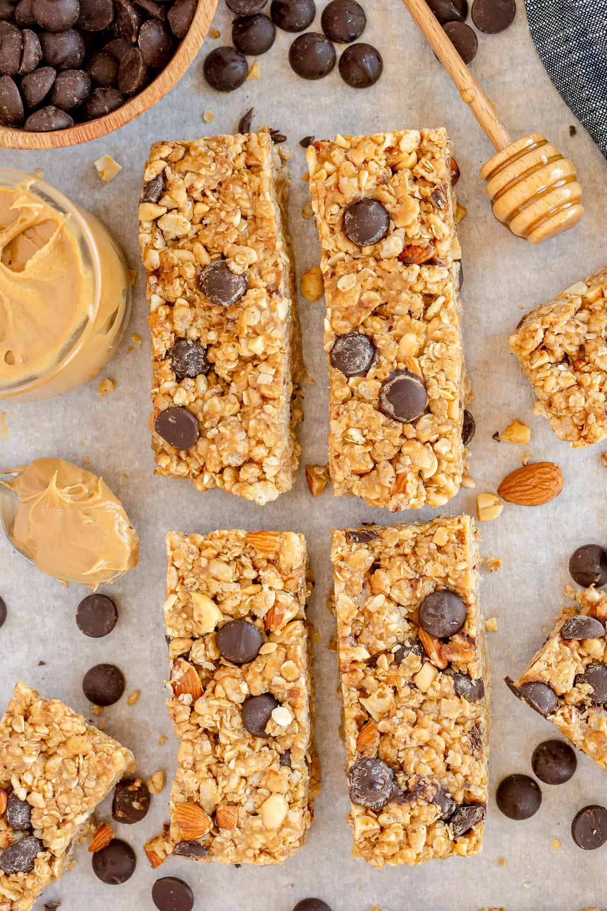 Four granola bars with chocolate chips on a board with peanut butter, honey, and almonds.