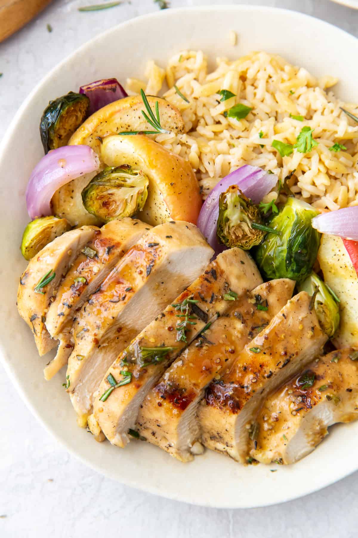 Sliced chicken with apple cider sauce in a white bowl with rice and vegetables.