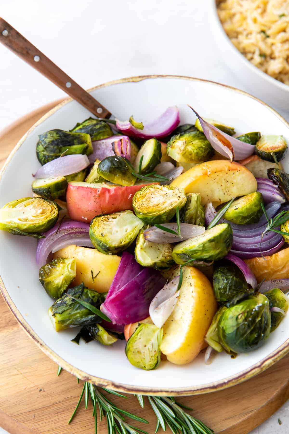 Roasted Brussels sprouts, apples, and red onion in a serving bowl with a spoon.