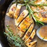 Sliced chicken and a whole breast in apple cider sauce in a skillet.