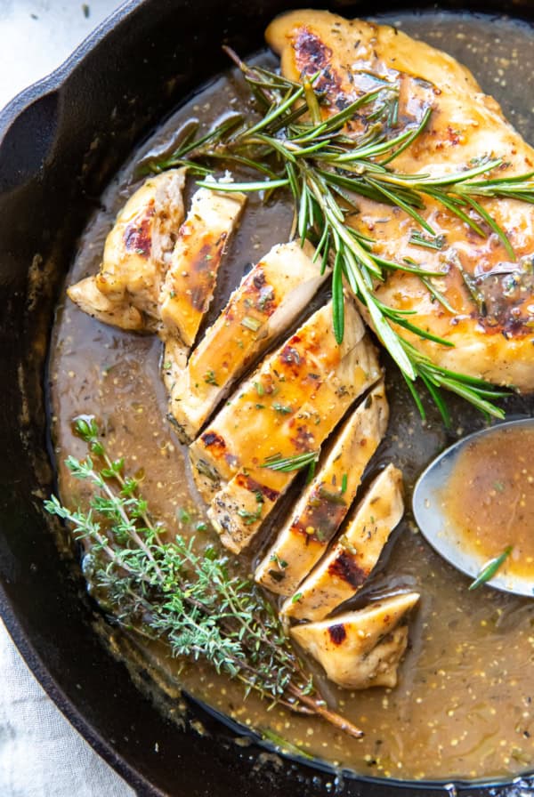 Sliced chicken and a whole breast in apple cider sauce in a skillet.