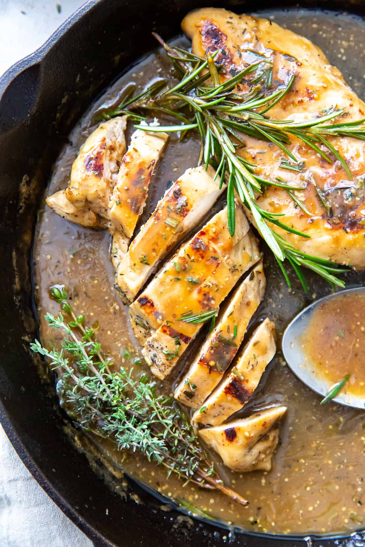 Sliced chicken and a whole breast in apple cider sauce in a skillet.