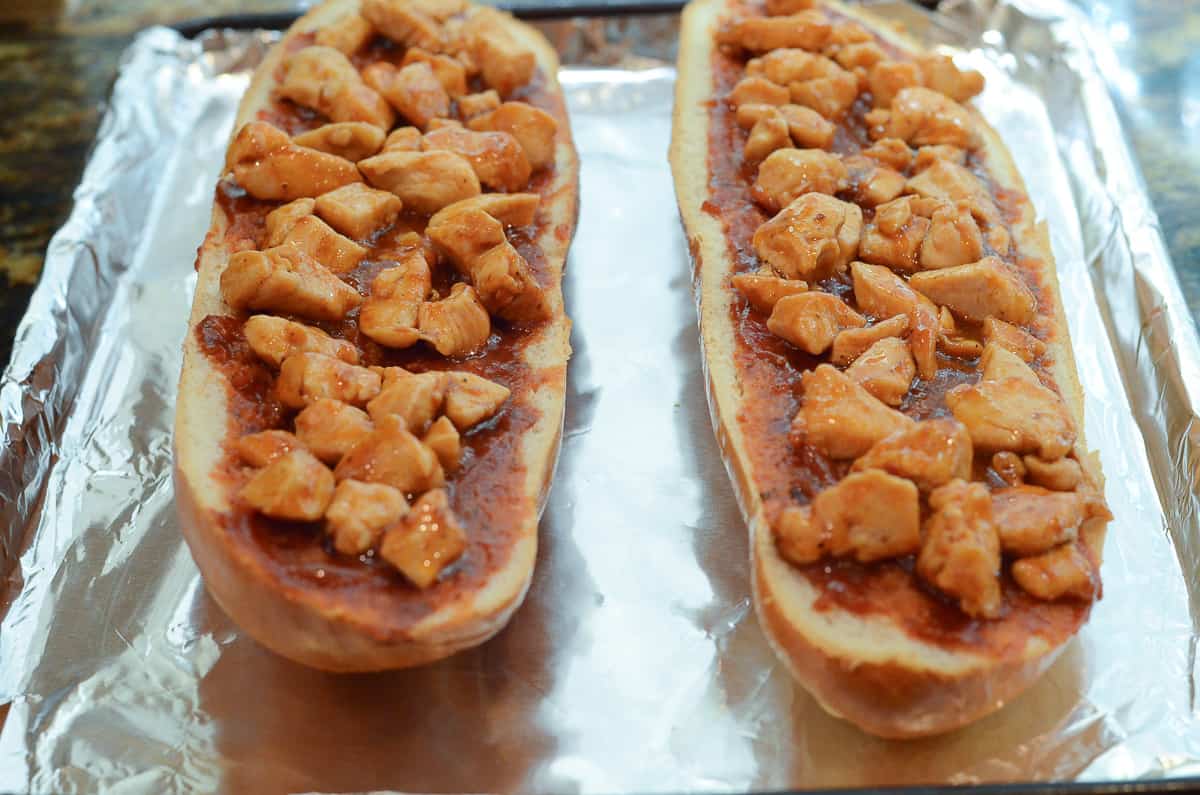 Two halves of a loaf of French bread coated with sauce and topped with chicken in BBQ sauce.