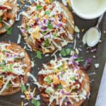 A bowl of salad dressing and a spoon rest on a baking sheet with tostadas.