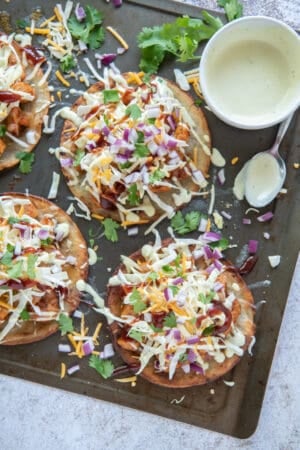 A bowl of salad dressing and a spoon rest on a baking sheet with tostadas.