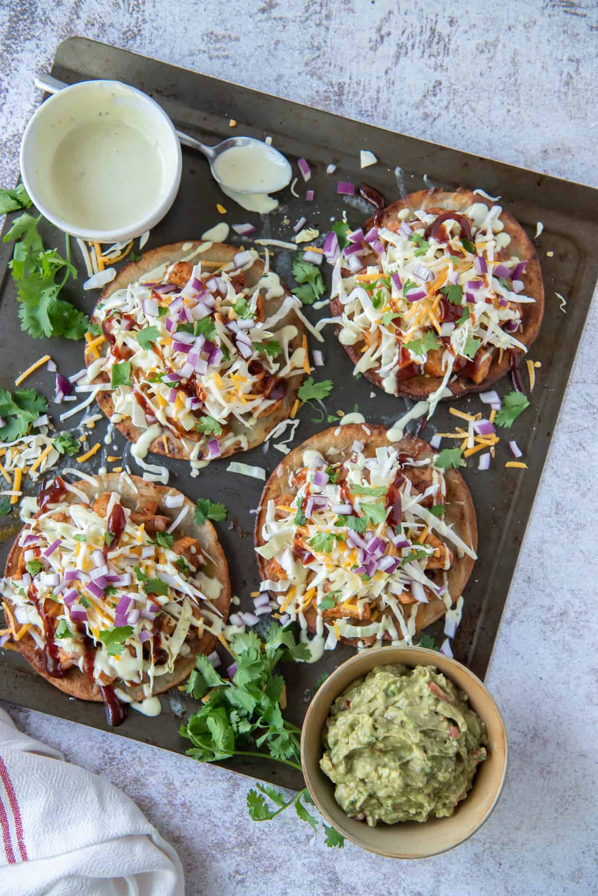Tostadas on a baking sheet with a bowl of guacamole and salad dressing.