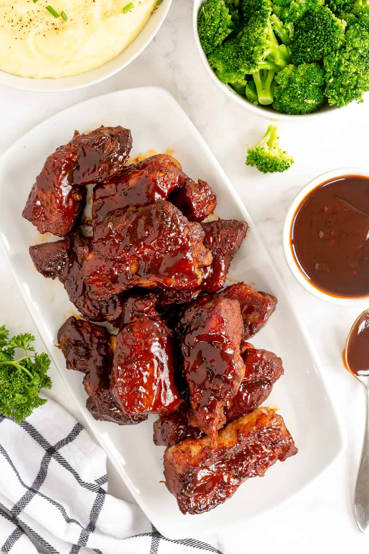 A platter of Country Style Ribs with BBQ sauce next to a bowl of mashed potatoes and broccoli.