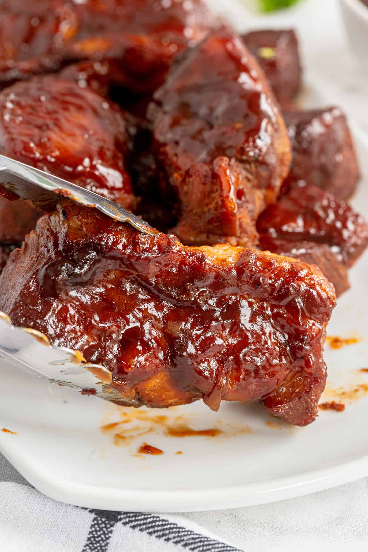 Metal tongs lifting a country style rib from a platter.