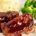 Two country style ribs with bbq sauce on a plate with mashed potatoes and broccoli.