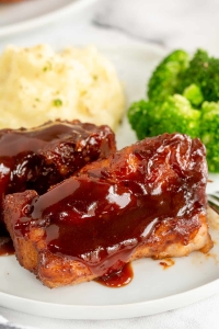 Two country style ribs with bbq sauce on a plate with mashed potatoes and broccoli.