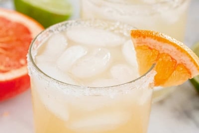 A paloma cocktail in a small glass with a grapefruit wedge on the rim.