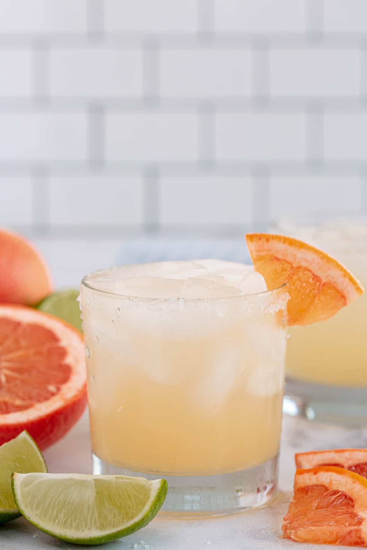 A paloma cocktail on a kitchen counter with grapefruit and lime wedges.