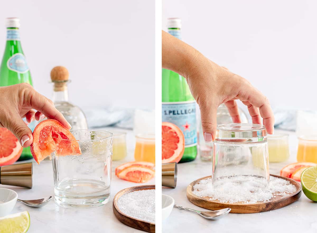 A hand rubs a grapefruit wedge around a glass rim and dips it in salt.