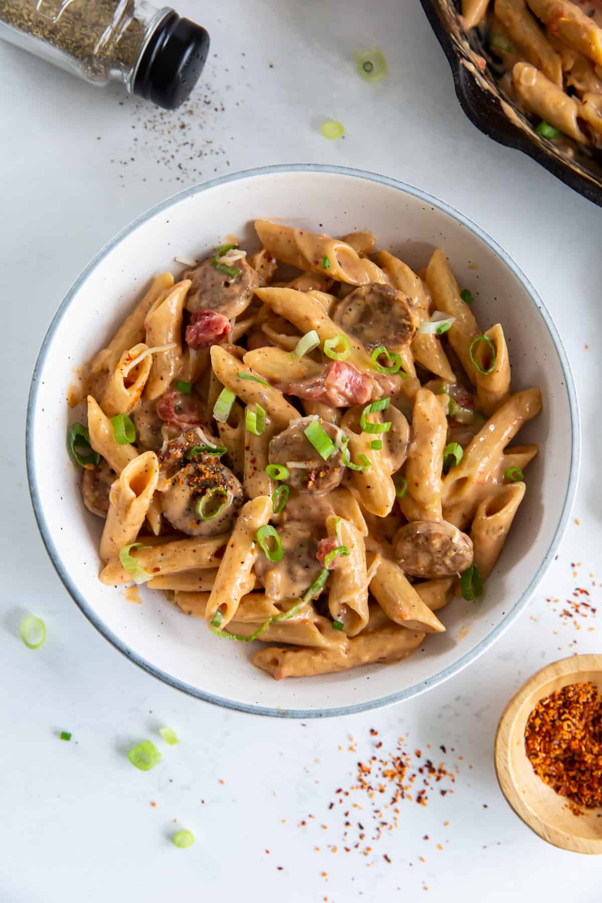 A serving of pasta with sausage in a white bowl.