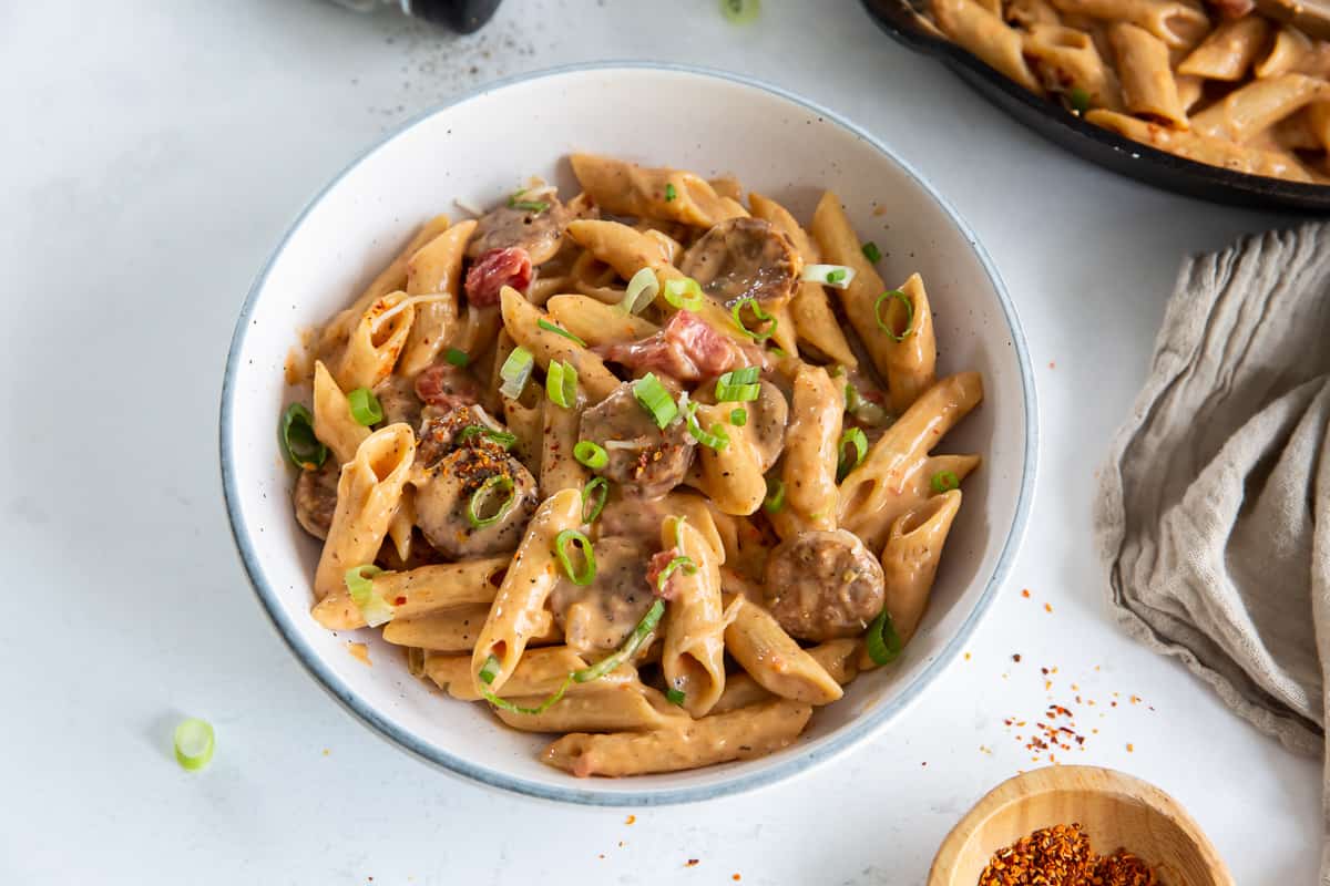 A serving of sausage pasta in a white bowl.