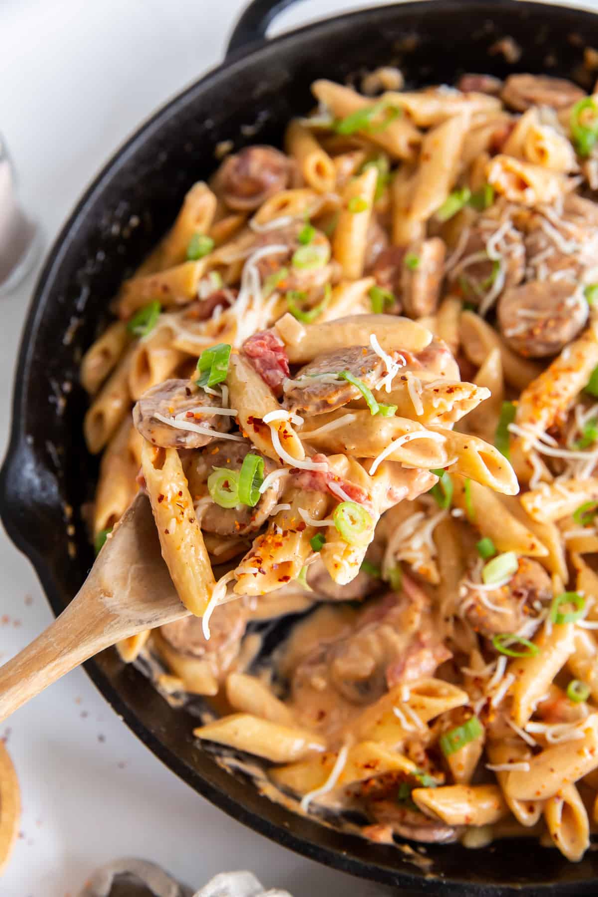 A wooden spoon scoops pasta from a skillet.