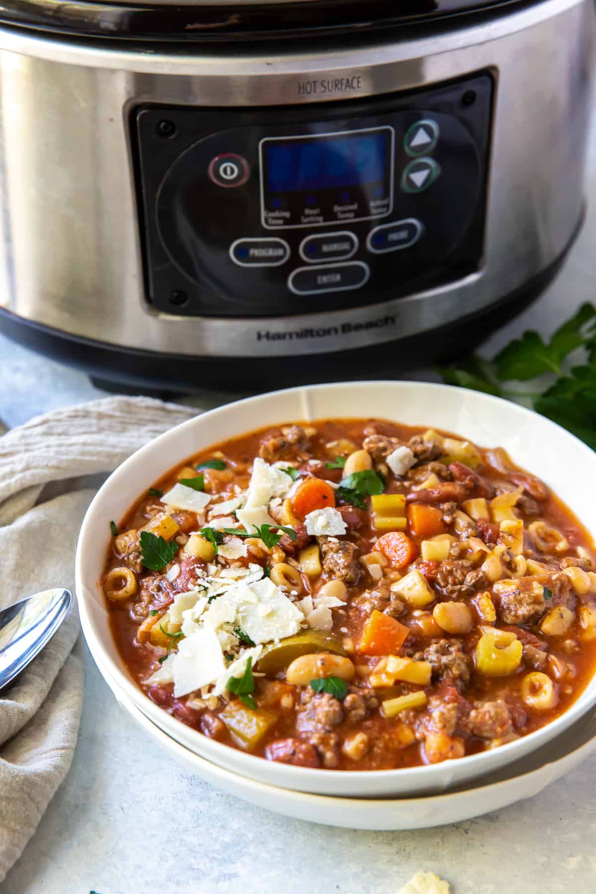 A bowl of minestrone soup in front of a slow cooker.