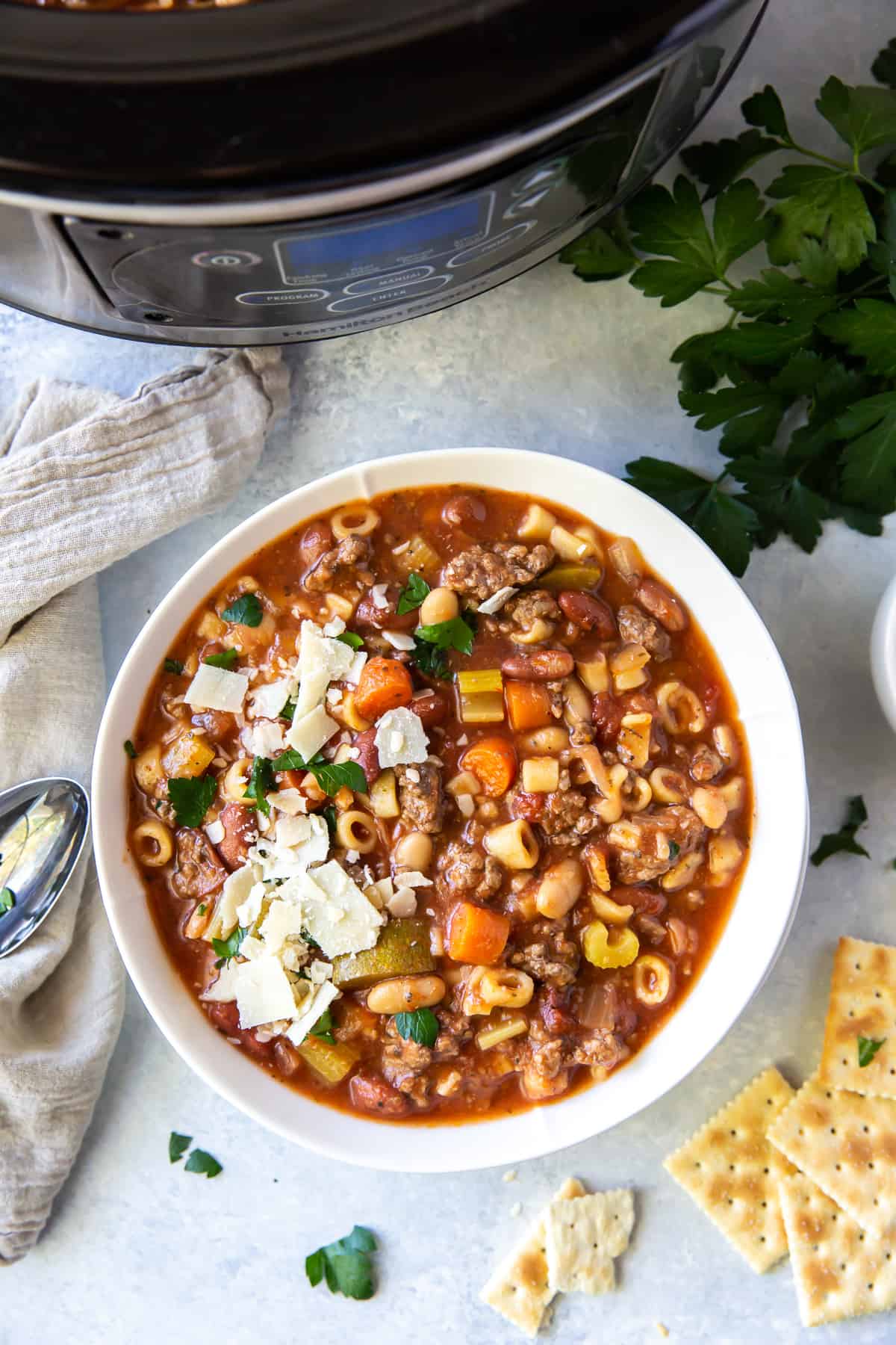 An over the top shot of a bowl of minestrone with ground beef in front of a slow cooker.