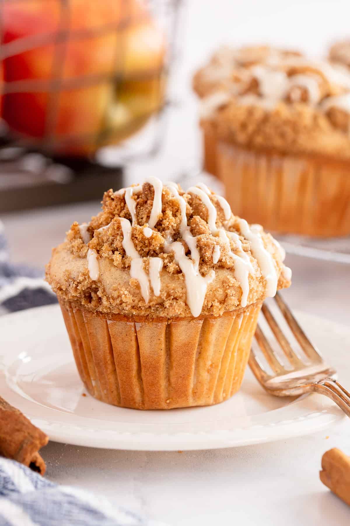 An apple muffin on a white plate in front of a crate of apples.